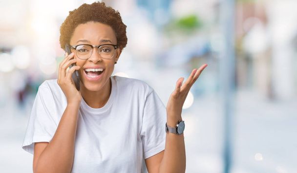 Joven mujer afroamericana hablando por teléfono sobre un fondo aislado muy feliz y emocionado, expresión ganadora celebrando la victoria gritando con una gran sonrisa y levantando las manos
 - Foto, Imagen