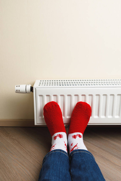 pernas com meias de veado de Natal vermelho na frente do radiador de aquecimento
 - Foto, Imagem