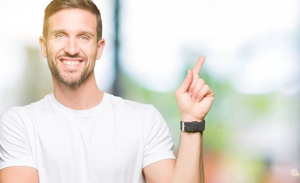 Handsome man wearing casual white t-shirt with a big smile on face, pointing with hand and finger to the side looking at the camera. - Fotoğraf, Görsel