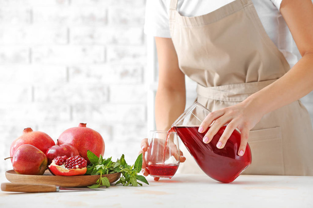 Vrouw gieten verse granaatappel sap in glas in de keuken - Foto, afbeelding