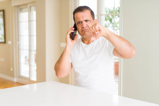 Keski-ikäinen mies soittaa käyttäen älypuhelin vihainen kasvot, negatiivinen merkki osoittaa pidä peukalot alas, hylkääminen käsite
 - Valokuva, kuva