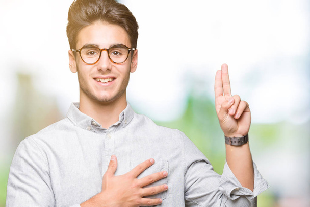 Mladý pohledný muž nosí brýle nad izolované na pozadí Swearing s rukou na hrudi a prstech, takže slib slib věrnosti - Fotografie, Obrázek
