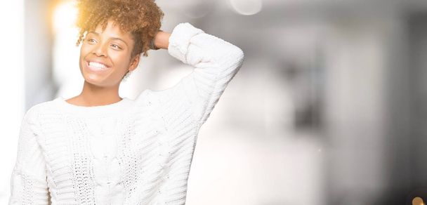 Linda jovem afro-americana vestindo camisola de inverno sobre fundo isolado Sorrindo confiante tocando o cabelo com mão para cima gesto, posando atraente
 - Foto, Imagem