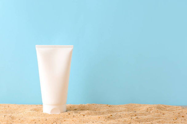Tube of sun protection cream on sand against color background - Photo, Image
