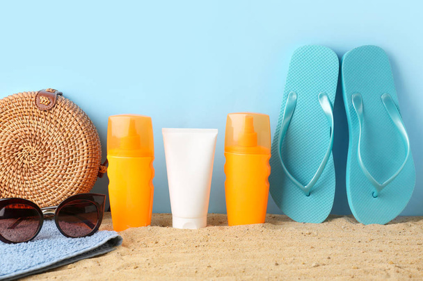 Beach bag, flip-flops, sunglasses and sun protection cream on sand against color background - Photo, Image