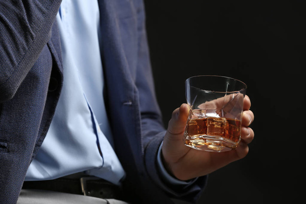 Επιχειρηματίας με ποτήρι ουίσκι σε σκοτεινό φόντο, κοντινό πλάνο - Φωτογραφία, εικόνα