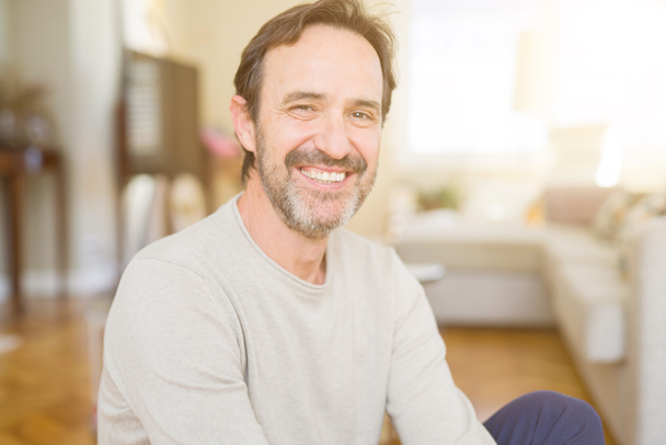 Handsome middle age man sitting on the floor smiling at the camera at home - Photo, Image