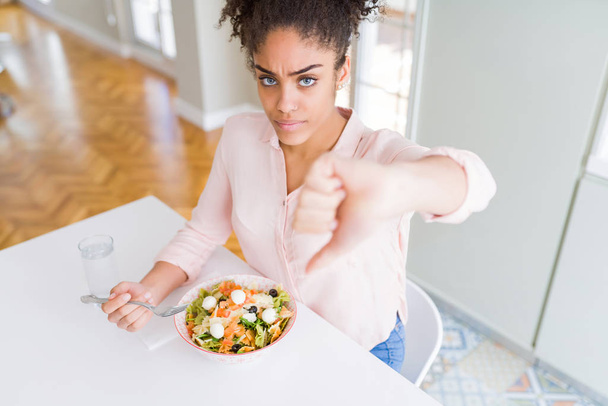 Jonge Afro-Amerikaanse vrouw die gezonde Pasta Salade met boos gezicht eet, negatief teken dat niet lijkt op duim omlaag, afwijzing concept - Foto, afbeelding