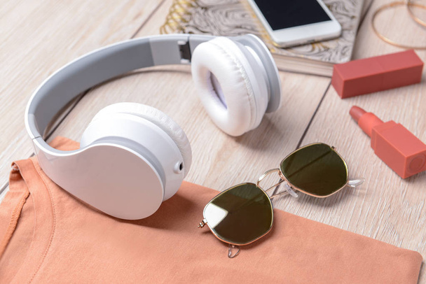 Modern headphones, sunglasses, t-shirt and cosmetics on wooden background - Photo, Image