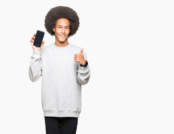 Молодой африканский американец с африканскими волосами показывает экран смартфона счастливым с большой улыбкой делает хорошо знак, палец вверх пальцами, отличный знак
 - Фото, изображение