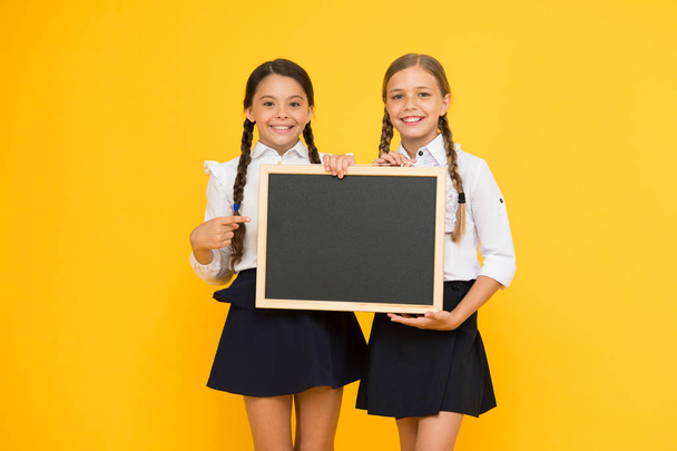Writing time. Little girls holding black writing surface on yellow background. Small children pointing finger at chalkboard for writing information. Blank board for writing, copy space - Valokuva, kuva