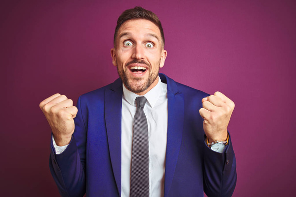 Young handsome business man over purple isolated background celebrating surprised and amazed for success with arms raised and open eyes. Winner concept. - Fotoğraf, Görsel