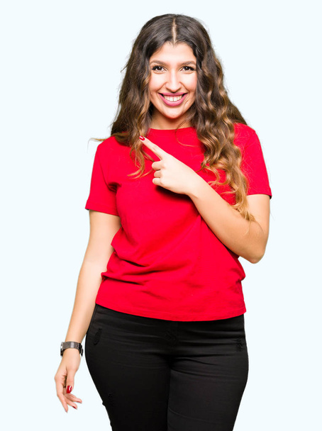 Молодая красивая женщина в повседневной футболке с улыбкой на лице, указывающей рукой и пальцем в сторону со счастливым и естественным выражением лица
 - Фото, изображение