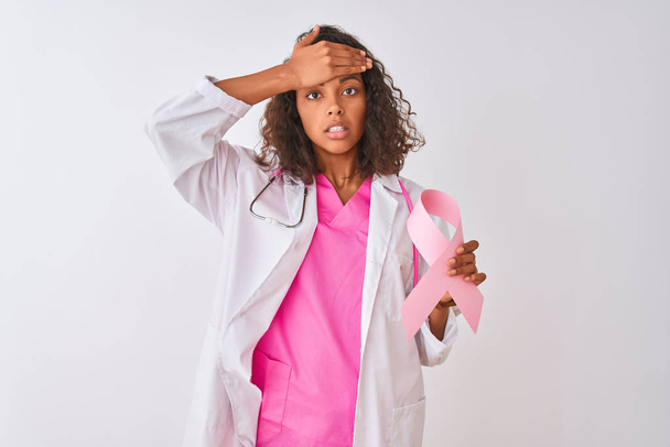 Young brazilian doctor woman holding cancer ribbon over isolated white background stressed with hand on head, shocked with shame and surprise face, angry and frustrated. Fear and upset for mistake. - Fotografie, Obrázek