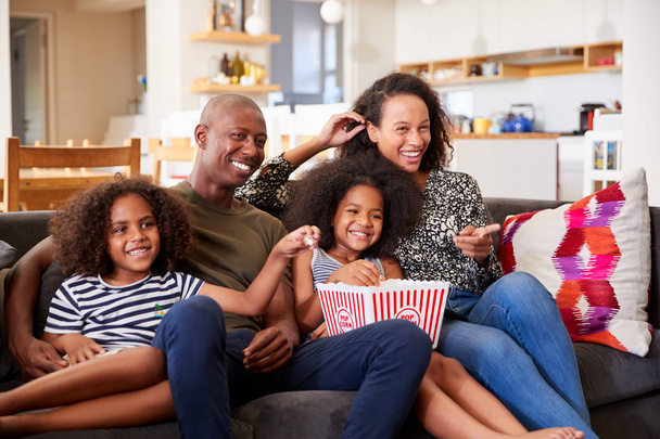 Family Sitting On Sofa At Home Eating Popcorn And Watching Movie Together - Foto, imagen