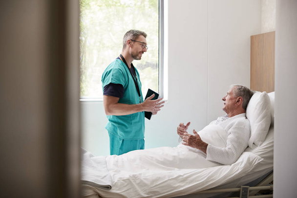 Χειρουργός με ψηφιακό δισκίο επισκέπτρια ανώτερο αρσενικό ασθενή σε νοσοκομείο κρεβάτι στη μονάδα Γηραί - Φωτογραφία, εικόνα