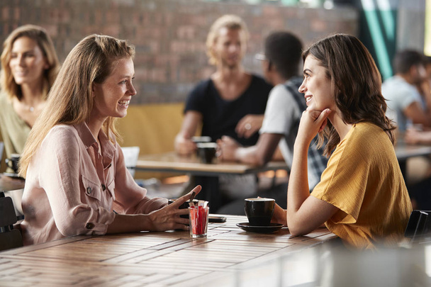 Two Female Friends Sitting At Table In Coffee Shop And Talking - Foto, Bild
