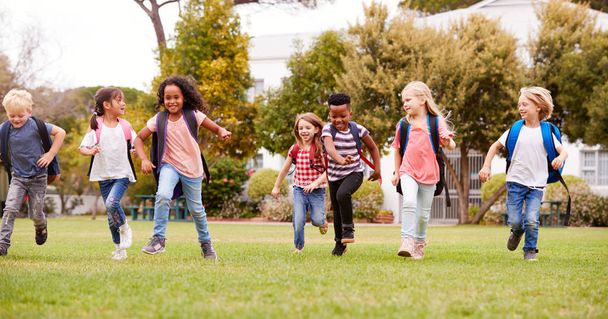 Excited Elementary School Pupils Running Across Field At Break Time - 写真・画像