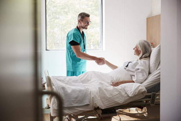 Návštěva chirurgu a třepání rukou s dospělou pacientkou v nemocničním loži - Fotografie, Obrázek