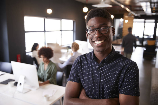 Milenial negro masculino creativo de pie en una oficina informal ocupado, sonriendo a la cámara
 - Foto, imagen