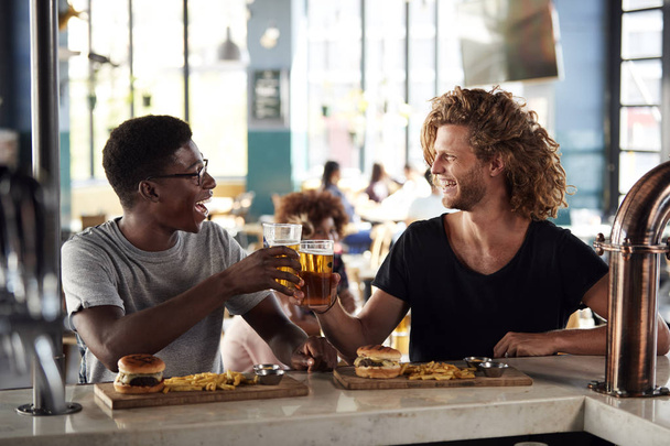 Two Male Friends Eating Food And Drinking Beer In Sports Bar - Foto, afbeelding