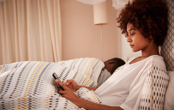 Millennial African American woman sitting up in bed using her smartphone, side view, close up - Foto, Imagem