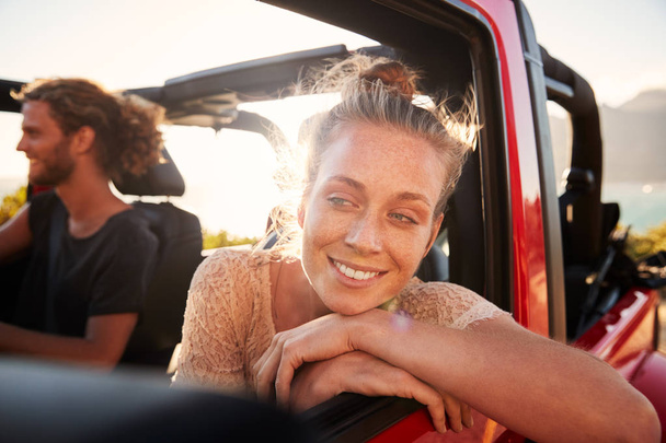 Millennial white couple on a road trip driving in open top car, women leaning on car door, close up - Foto, afbeelding