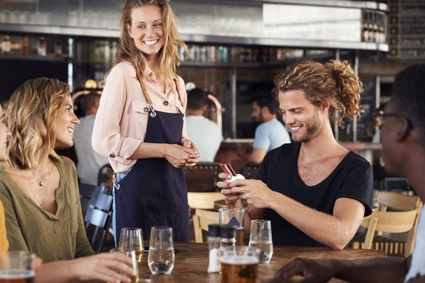 Waitress Holds Credit Card Machine As Customer Pays Bill In Bar Restaurant - Foto, afbeelding