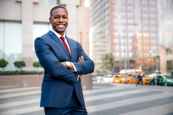 stolzer erfolgreicher Geschäftsmann aus Afrika, der selbstbewusst mit verschränkten Armen in Downtown, Finanzgebäuden und Wolkenkratzern steht - Foto, Bild