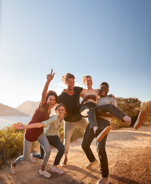 Five millennial friends on a road trip have fun posing for photos on a coastal path, full length - Foto, afbeelding