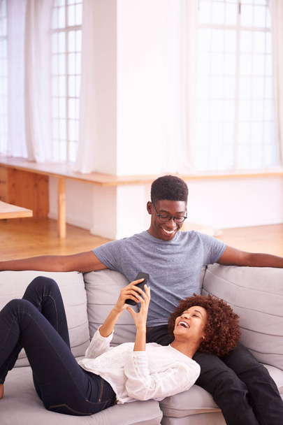 Young Couple Relaxing On Sofa At Home Looking At Mobile Phone Together - Foto, Bild