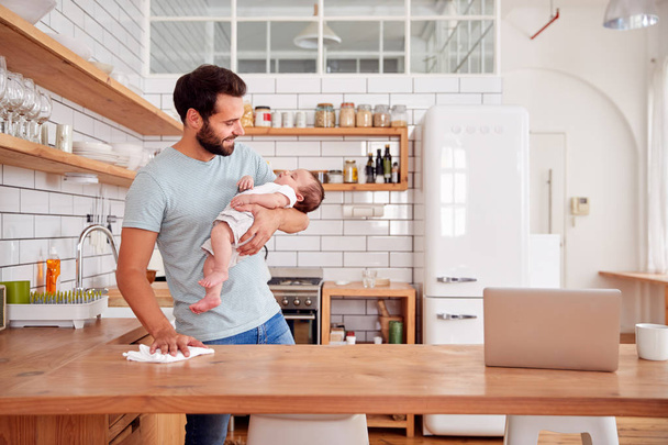 Multi-Tasking Father Holding Sleeping Baby Son And Cleaning In Kitchen - Photo, Image