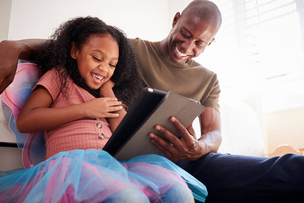Father With Daughter Sitting On Bed In Child Bedroom Using Digital Tablet Together - Фото, изображение