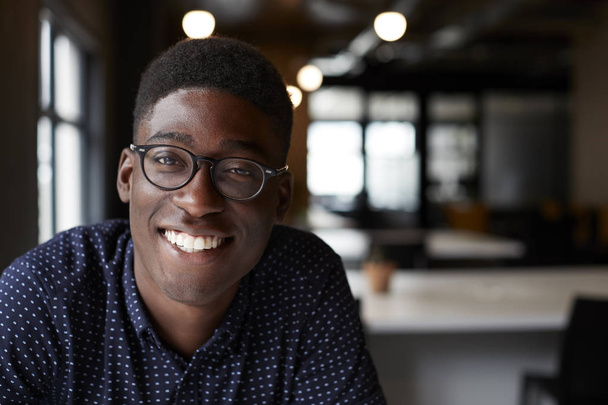 Millennial black male creative sitting at a desk in an office smiling to camera, close up - Foto, immagini