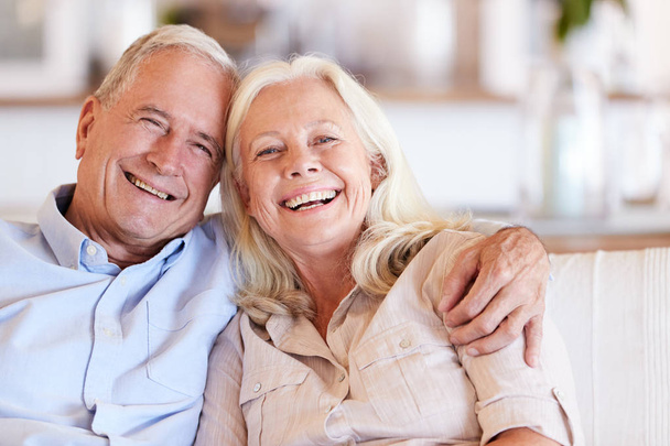 Happy senior white couple sitting at home embracing and smiling to camera, front view, close up - Foto, afbeelding
