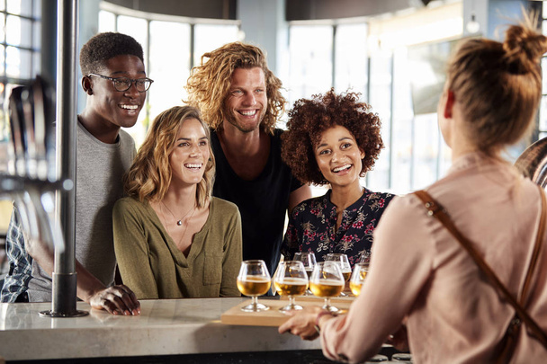 Waitress Serving Group Of Friends Beer Tasting In Bar - Фото, зображення