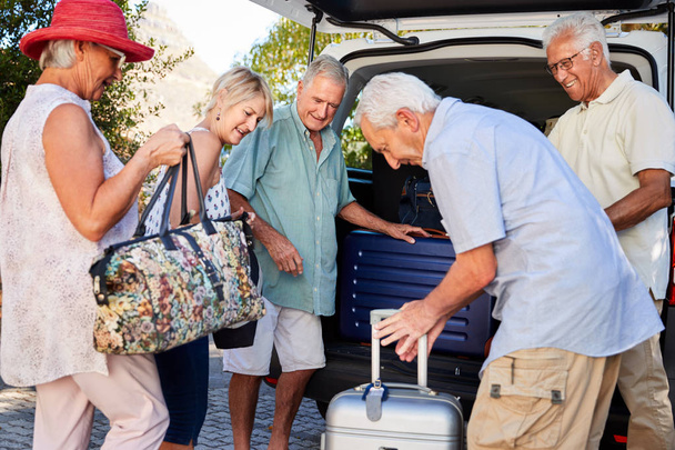 Group Of Senior Friends Loading Luggage Into Trunk Of Car About To Leave For Vacation - Foto, imagen