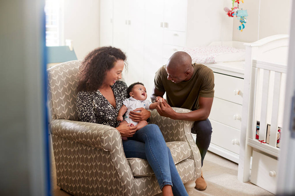 Loving Parents Sitting In Chair Cuddling Baby Son In Nursery At Home - Foto, imagen