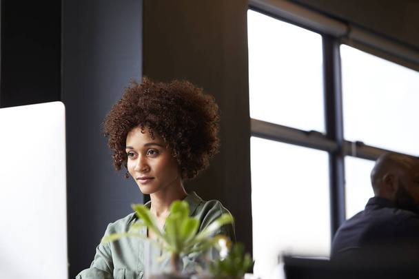 Millennial musta nainen luova istuu pöydän ääressä toimistossa tietokoneella, lähikuva
 - Valokuva, kuva