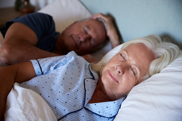 Senior white couple lying asleep in their bed, waist up, close up - 写真・画像