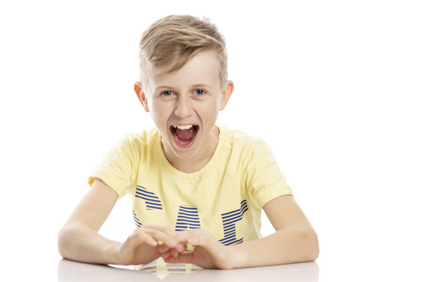 Teen guy screaming angrily while sitting at the table. Isolated over white background.  - Foto, imagen
