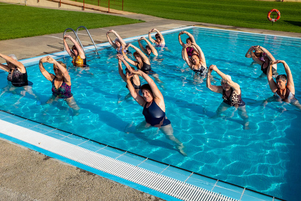 Action-Aufnahme von Seniorinnen bei gemeinsamen Wassergymnastikübungen im Freibad. - Foto, Bild