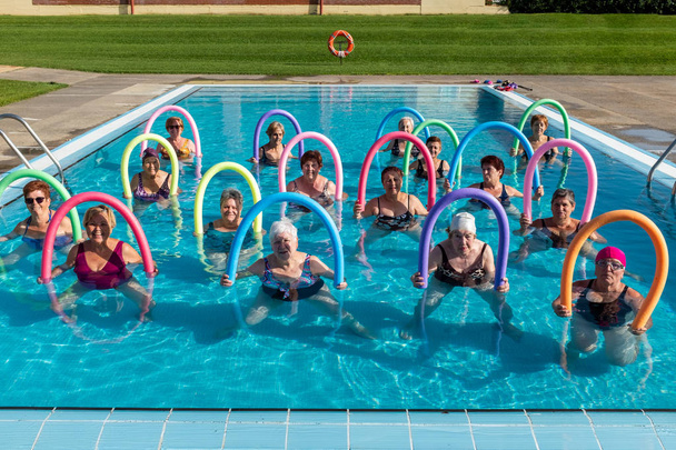 Vooraanzicht portret van senior aqua gym klas met schuim noedels. Sportieve dames staan samen in het buitenzwembad. - Foto, afbeelding