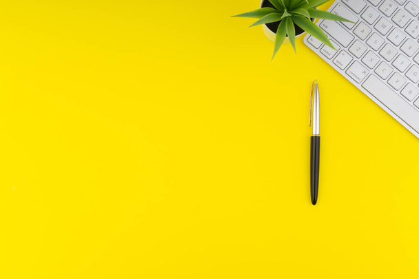 Vlakke lay View van Office tafel Bureau. Werkruimte met toetsenbord, zwarte pen en decoratie bloem op gele achtergrond. Concept van bedrijfs-en kopieer ruimte - Foto, afbeelding