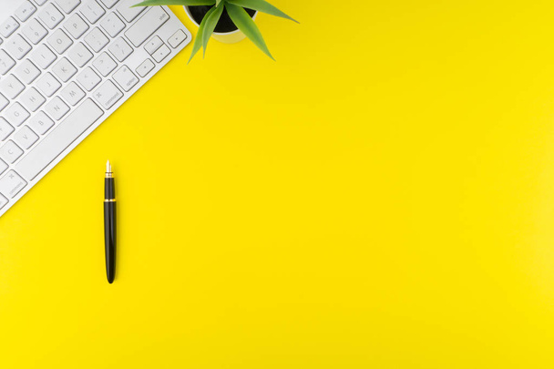 Vlakke lay View van Office tafel Bureau. Werkruimte met toetsenbord, zwarte pen en decoratie bloem op gele achtergrond. Concept van bedrijfs-en kopieer ruimte - Foto, afbeelding