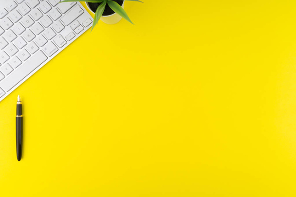 オフィステーブルデスクの平らな平面図。黄色の背景にキーボード、黒ペンと装飾花とワークスペース。ビジネスとコピースペースの概念 - 写真・画像