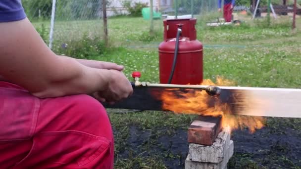 ein Mann verbrennt Holzbohlen mit Propan in alter japanischer Technologie und schafft so Verkleidungsmaterial für den Hausbau - Filmmaterial, Video