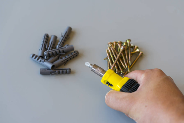 Male hand with a screwdriver for screws and dowels on a gray background. Repair and maintenance concept - Photo, Image