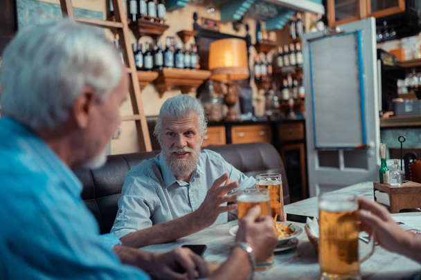 Bearded grey-haired mature man speaking with friends - Фото, зображення
