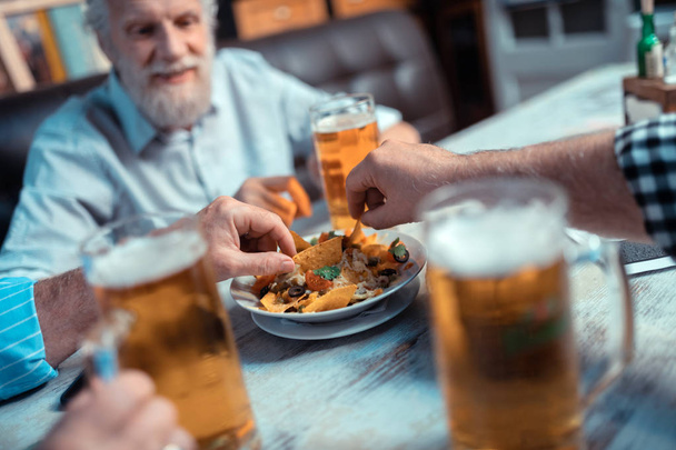 Kypsät miehet ottavat nachoja juodessaan olutta
 - Valokuva, kuva